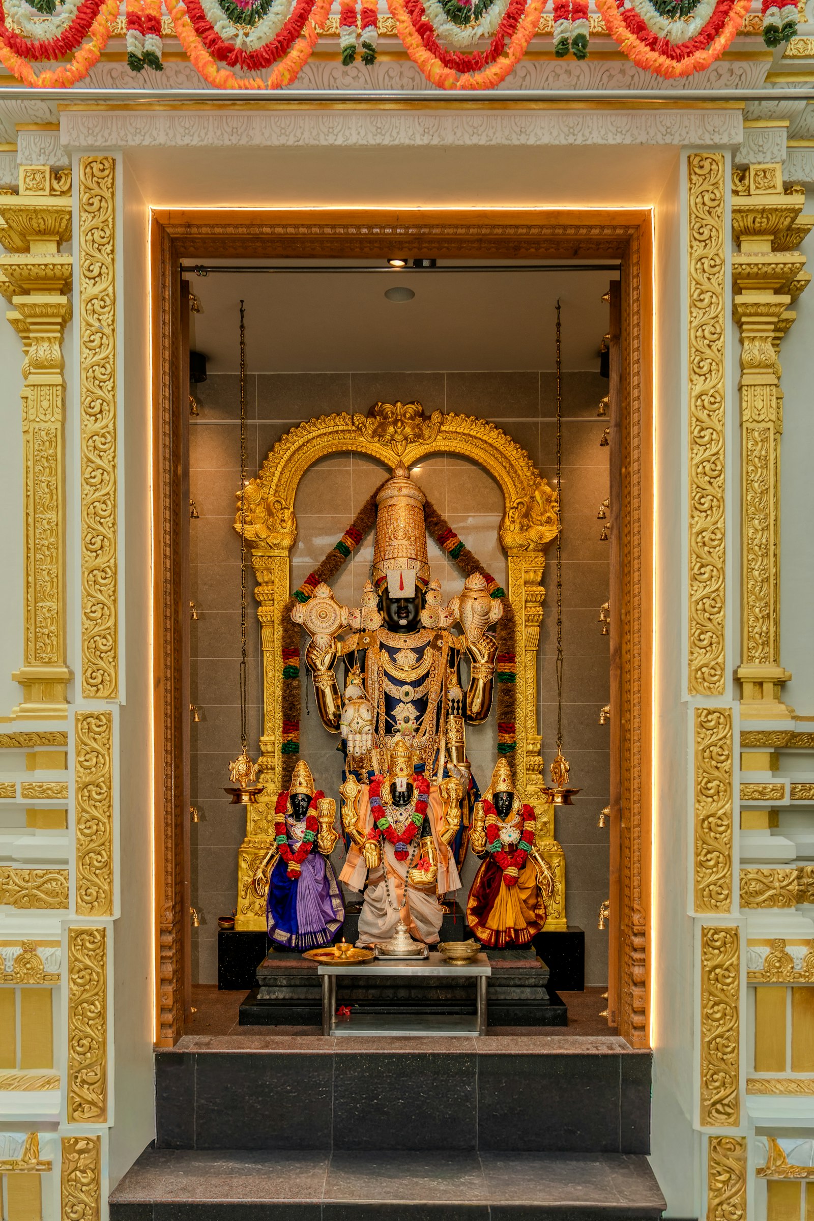 A consecrated deity adorned with garlands and gold, at the heart of a home shrine