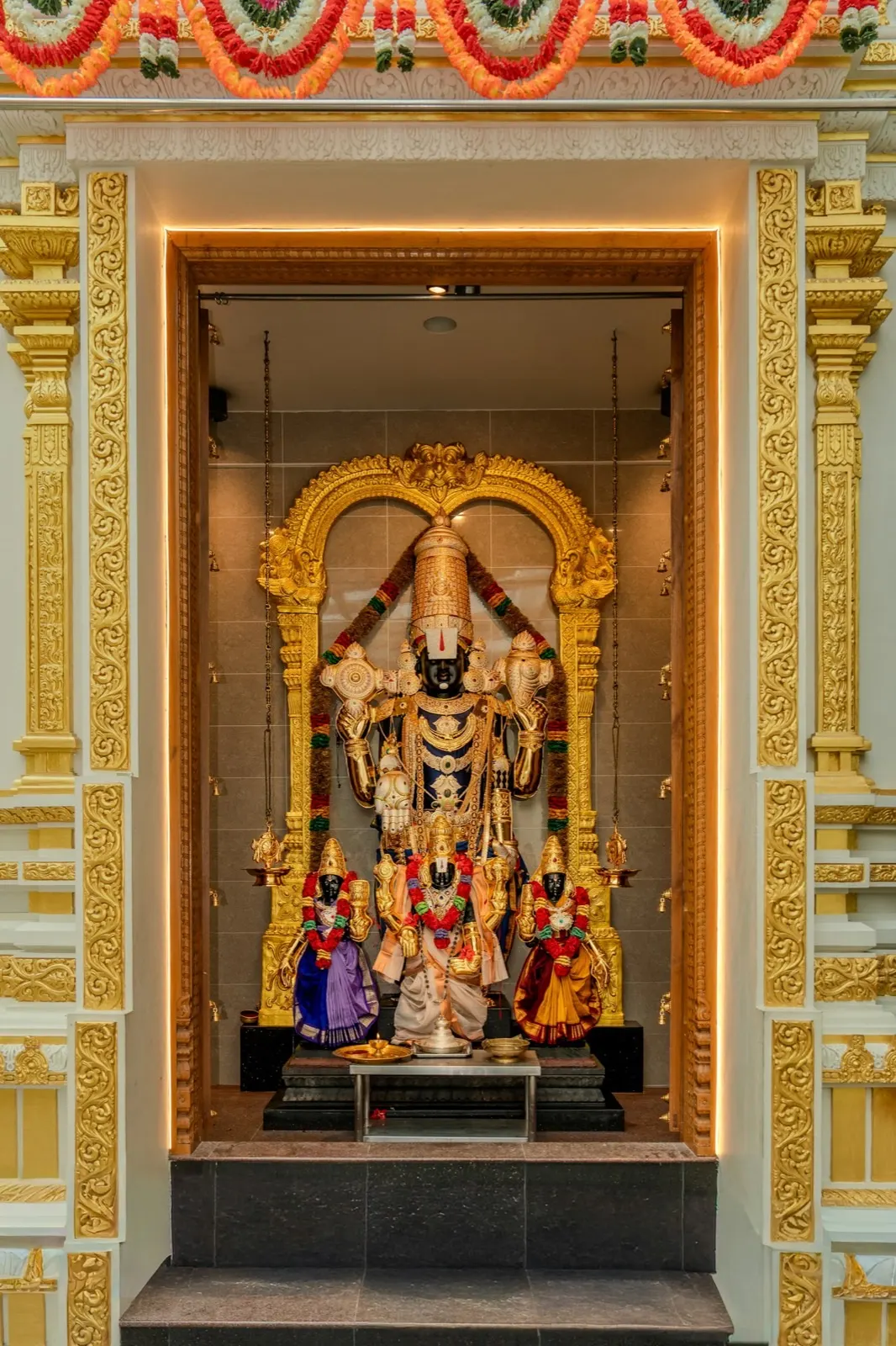 A consecrated deity adorned with garlands and gold, at the heart of a home shrine