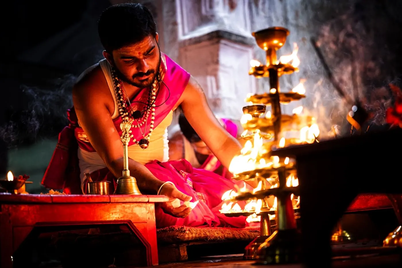A Pujari performing a pooja ceremony with a diya, incense and offerings